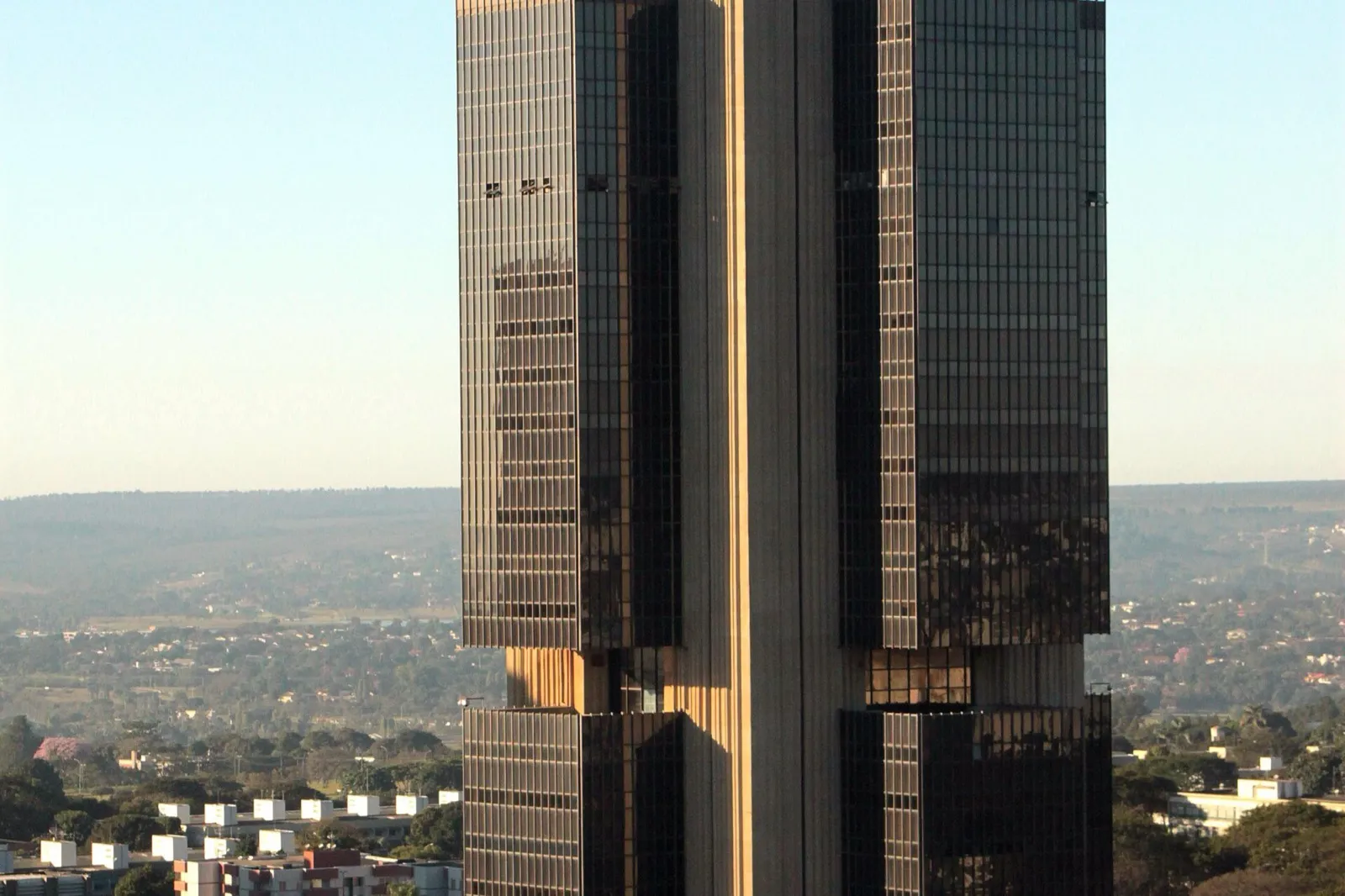 Fachada do edifício-sede do Banco Central do Brasil, em Brasília, com torre de vidro escuro e concreto sob céu azul