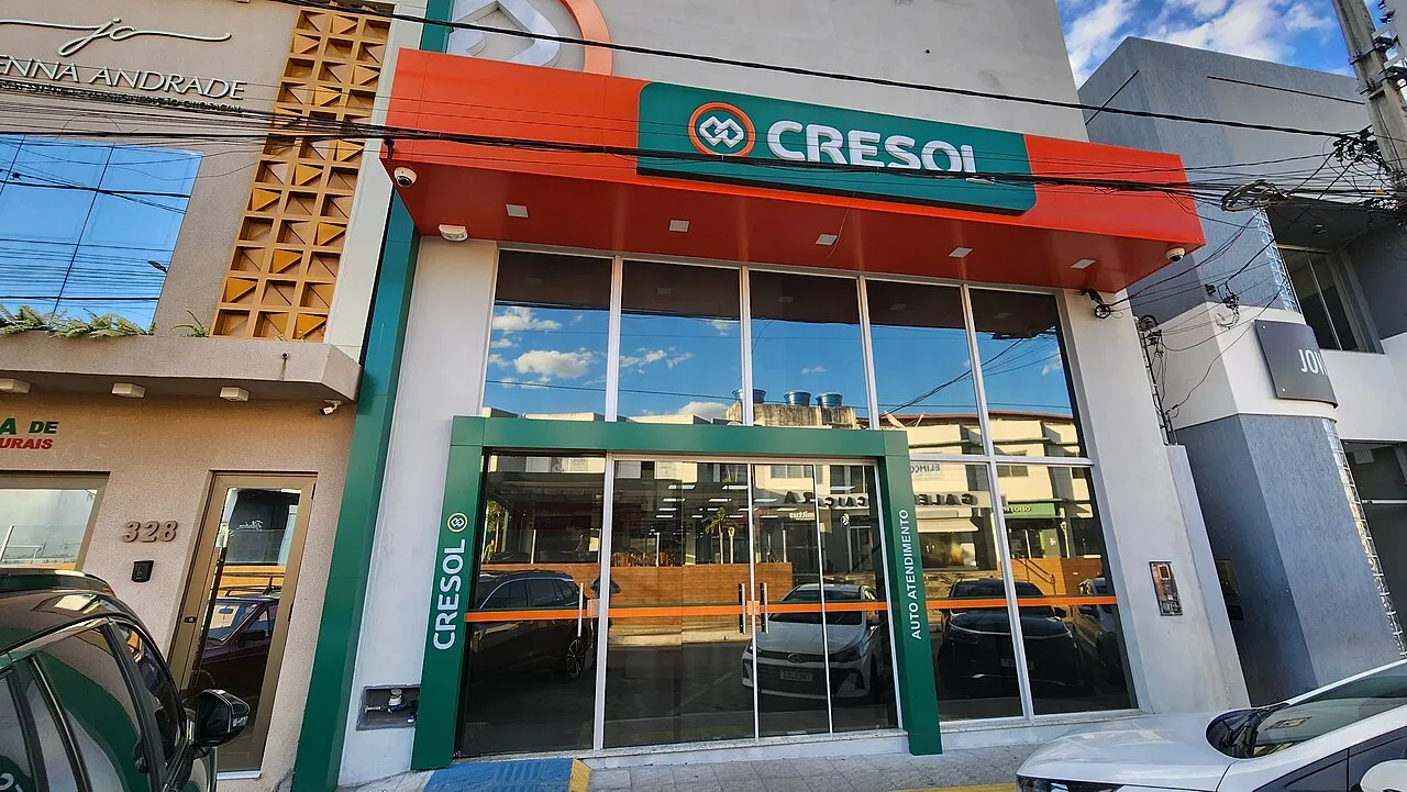 Fachada de vidro de uma agência da cooperativa de crédito Cresol, com letreiro verde e laranja e porta de autoatendimento