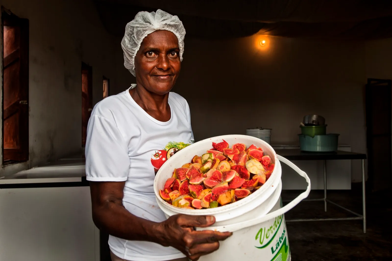 Agricultora de Conceição do Coité, na Bahia, segura balde com frutas cortadas em uma sala de processamento