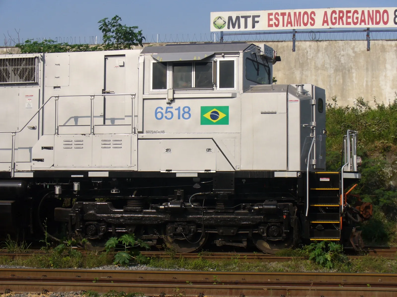 Locomotiva de carga cinza, com o número 6518 e a bandeira do Brasil na lateral, em uma linha férrea