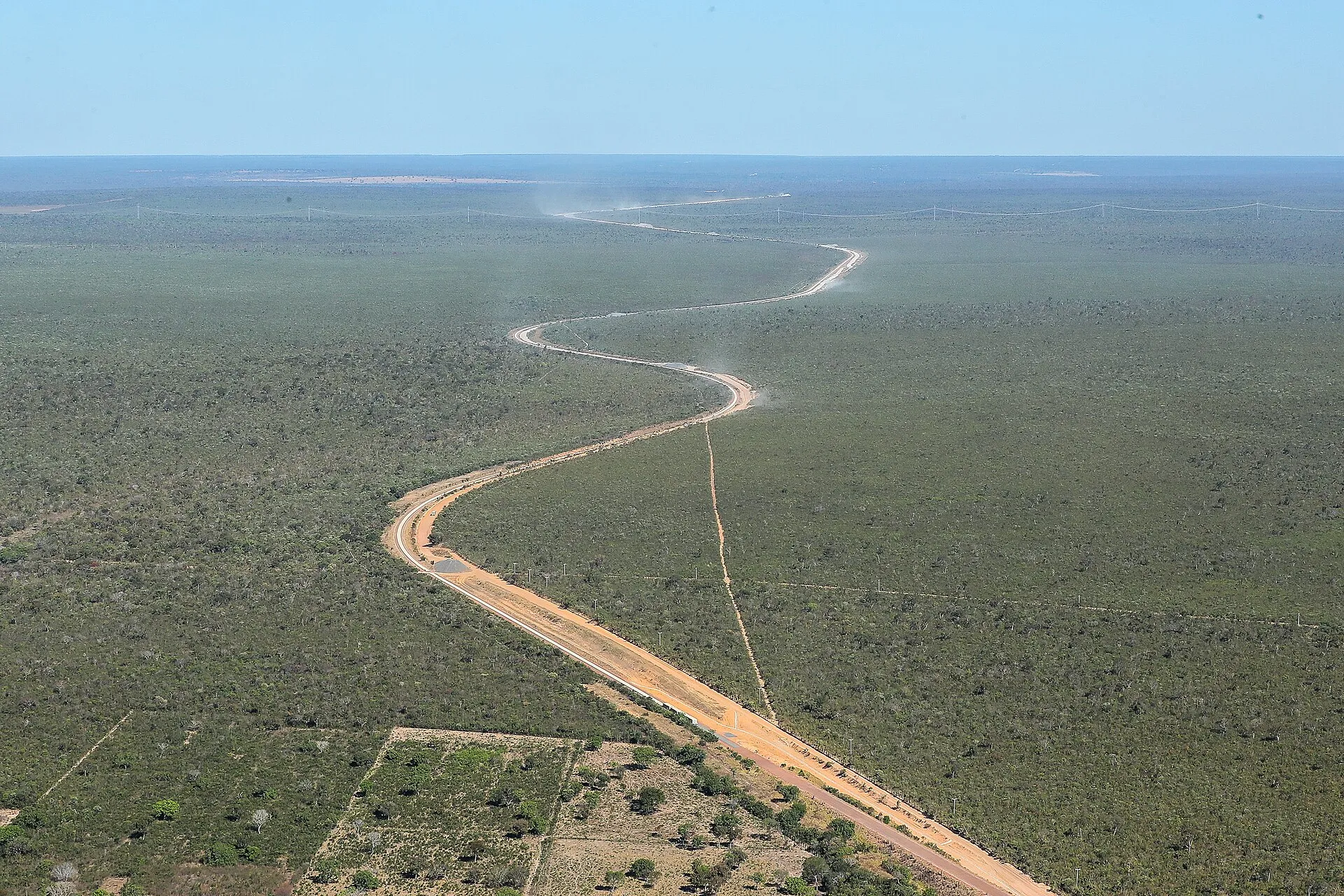 Vista aérea de uma faixa de terra em curva no cerrado, com postes de uma linha ao fundo, em área de obras da Fiol